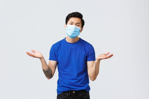 Different emotions, social distancing, self-quarantine on coronavirus concept. Unbothered and indifferent asian guy in medical mask asking so what, spread hands sideways shrugging, dont care.