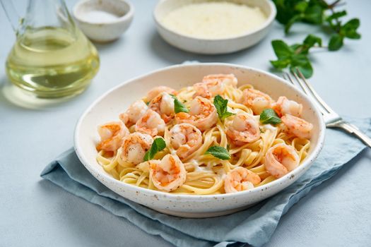 Pasta spaghetti with grilled shrimps, bechamel sauce, mint leaf on blue table, italian cuisine, side view