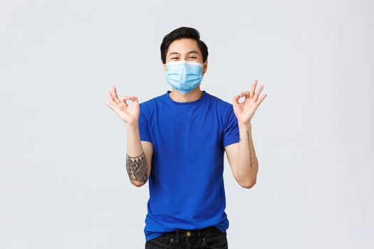 Different emotions, social distancing, self-quarantine on covid-19 and lifestyle concept. Glad happy asian man in medical mask, show okay sign, approve and like idea, recommend product.