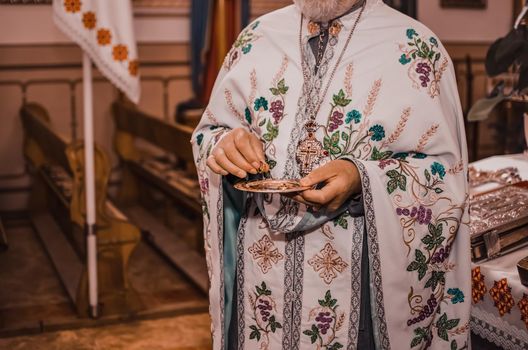 A white-robed priest with a cross on his chest holds a saucer with lighted gold wedding rings.