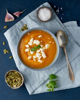 Pumpkin cream soup with a sheep cheese, autumn homemade food, dark blue background, top view, vertical. Fodmap diet, lchf. Vegetarian menu, clean eating recipe