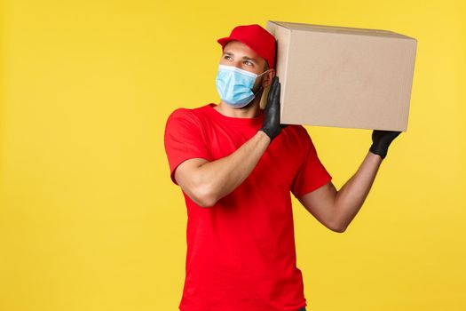 Express delivery during pandemic, covid-19, safe shipping, online shopping concept. Young courier protect clients order, carefully holding package on shoulder, look upper left corner, medical mask.