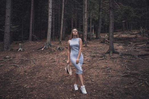 Slavic tanned fair-haired young girl with a boater hat on nature. Traveler tourist in a dark forest. constant tone of clothes. dark brown background