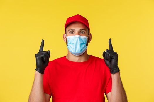 Covid-19, delivery orders, shopping, contactless payment and social distancing concept. Excited and impressed courier, male employee in medical mask and uniform, pointing fingers up astonished.