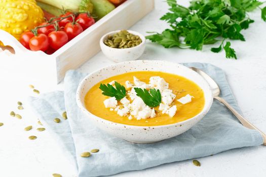 Pumpkin cream soup with feta cheese, autumn homemade food, white background, closeup seasonal vegeterian dish