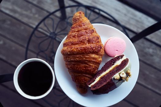 Breakfast with croissant and dessert, coffee or tea in plastic mug, in the village, outdoors, nature. Selective focus.