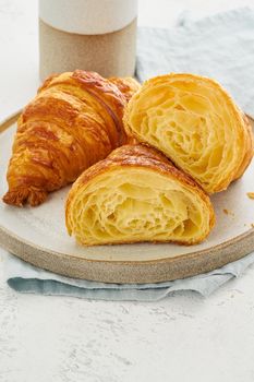 Two delicious croissants on plate and hot drink in a mug. Croissant sectional view, showing layers of gingerbread dough. Morning French breakfast with freshly baked pastries. Light gray background.