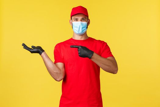 Express delivery during pandemic, covid-19, safe shipping, online shopping concept. Happy good-looking courier, enthusiastic delivery employee in uniform, pointing at hand holding your product.