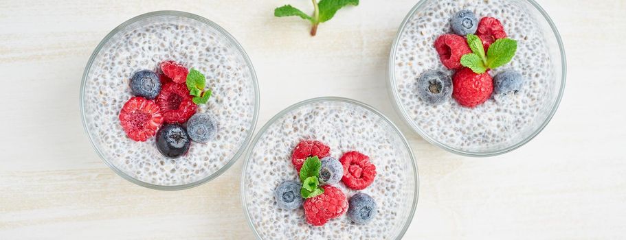 Long banner with Chia pudding with fresh berries raspberries, blueberries. Three glass, top view