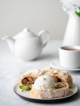 Apple strudel with ice cream and cinnamon. Baked cake and tea, delicious dessert on the table. Side view, vertical