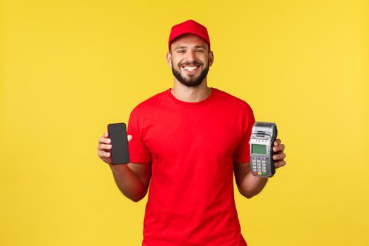 Contactless payment, online delivery, internet shopping concept. Friendly smiling employee, courier in red uniform showing smartphone screen and POS terminal, standing yellow background.