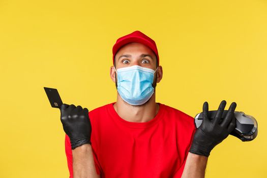 Covid-19, delivery orders, shopping, contactless payment and social distancing concept. Close-up of happy employee, courier in red uniform and medical mask, using credit card with POS terminal.