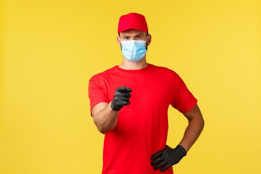 Express delivery during pandemic, covid-19, safe shipping, online shopping concept. Confident courier in red uniform, medical mask and gloves, pointing finger camera, promote logistic company.