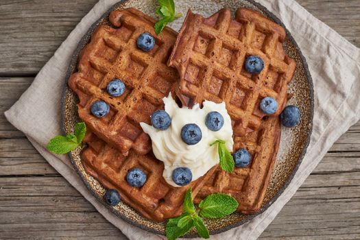 Chocolate banana waffles with blueberries, on dark wooden the old table. Top view, close up