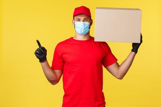 Express delivery during pandemic, covid-19, safe shipping, online shopping concept. Handsome delivery guy, courier holding box with package and pointing upper left corner, wear medical mask.