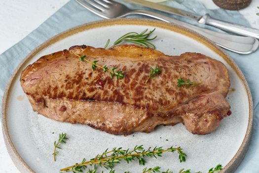 Keto ketogenic diet beef steak, striploin on gray plate on white background. Paleo food recipe with whole big piece of meat and a seasoning. Close up, side view