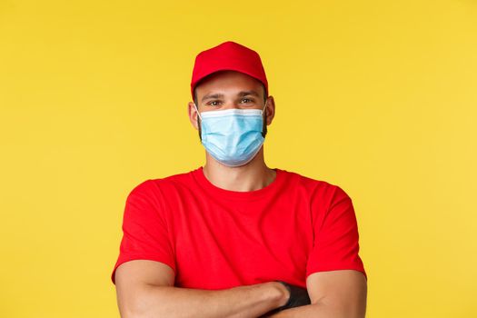 Covid-19, delivery orders, shopping, contactless payment and social distancing concept. Close-up of carefree handsome courier looking optimistic, cross arms, wear medical mask, working on coronavirus.
