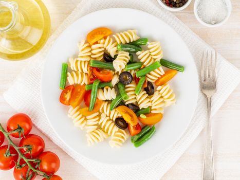 Italian salad with fusilli paste tomatoes, olives, green beans, top view, close up.