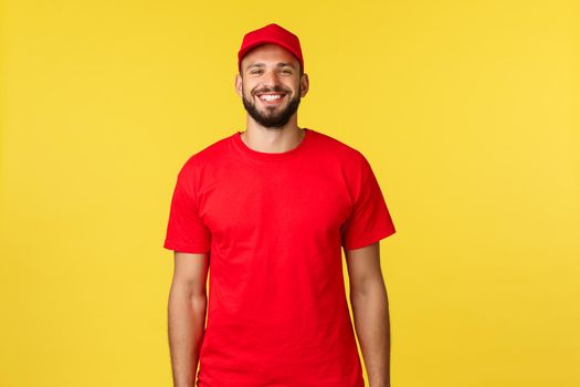 Express mail delivery, package transfer and logistics concept. Cheerful young bearded courier in red uniform cap and t-shrit, smiling happy as standing yellow background.