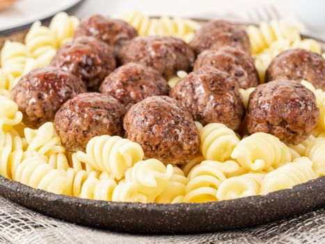 Swedish meatballs with fusilli paste on white wooden table, side view