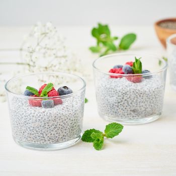 Chia pudding with fresh berries raspberries, blueberries. Two glass, light wooden background, side view, flowers, close up