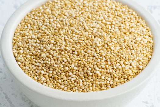 Quinoa seed in a white bowl on white background. Dried cereals in cup, vegan food, fodmap diet. Side view, close up.