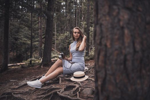 Slavic tanned fair-haired young girl with a boater hat on nature. Traveler tourist in a dark forest. constant tone of clothes. dark brown background