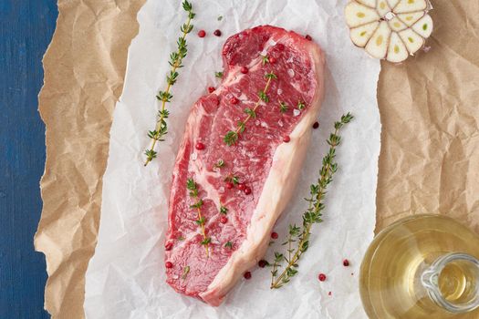 Big whole piece of raw beef meat, striploin on white parchment paper on craft background, zero waste packing. Seasoning steak with salt, blue table