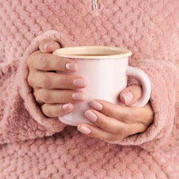 hands holding a cup of tea or coffee, pink home cozy jacket, beautiful pink manicure, home style, autumn morning, close up