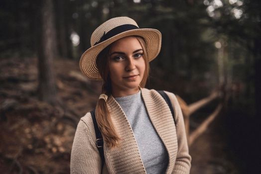 Slavic tanned fair-haired young girl with a boater hat on nature. Traveler tourist in a dark forest. constant tone of clothes. dark brown background