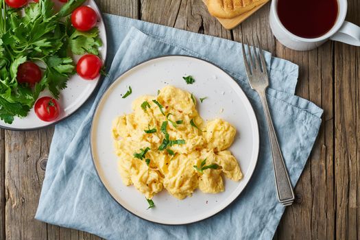 Scrambled eggs, omelette, top view. Breakfast with pan-fried eggs, cup of tea, tomatoes on the old rustic wooden table