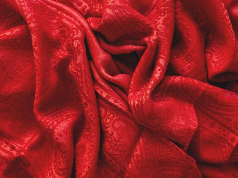 Bright red scarf. Folded warm accessory. Crumpled textile background with ornament. Top view on fabric backdrop.