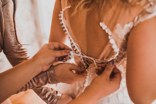 The back of the bride in a wedding dress. Mom's and woman's hands help fasten the clasps at the back.