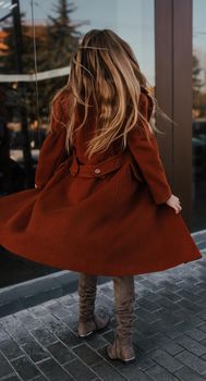 young blonde woman in autumn clothes walks on street background shop windows. Street style Fashion 2021 Winter Spring Terracotta Coat Woolen Cashmere Suede Over Knee Boots White Golf