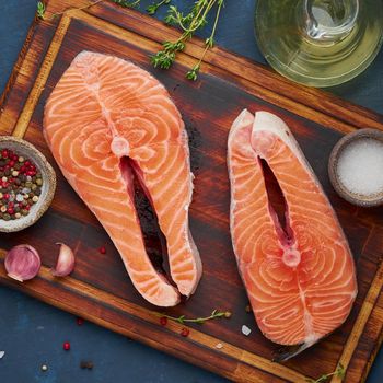 Two salmon steaks, fish fillet, large sliced portions on chopping board on dark table. Top view, close up