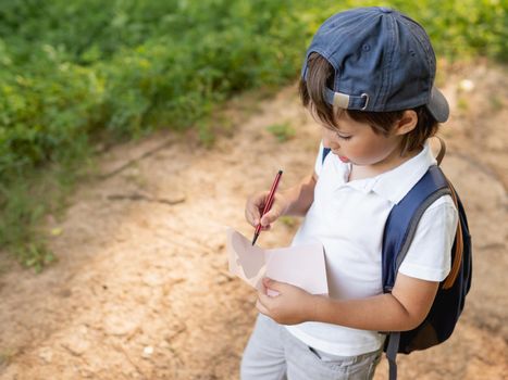 Mindful boy writes something in notebook while walking in forest. Exploring nature. Summer outdoor recreation. Healthy lifestyle.