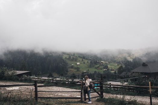 young thin woman traveler near old fence against background of high Carpathian mountains in fog