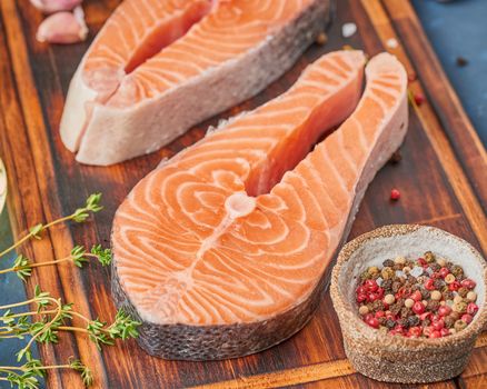 Two salmon steaks, fish fillet, large sliced portions on chopping board on dark table. Food background