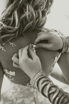 The back of the bride in a wedding dress. Mom's and woman's hands help fasten the clasps at the back.