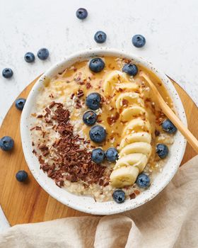 Oatmeal rustic porridge with blueberry, bilberry, blackberry, banana, chocolate and nut honey pasta, dash diet, wooden white background top view