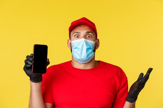 Covid-19, delivery, shopping, contactless payment and social distancing concept. Close-up of astonished, excited courier talking about new application, show mobile phone screen, wear medical mask.