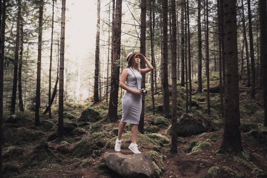 Slavic tanned fair-haired young girl with a boater hat on nature. Traveler tourist in a dark forest. constant tone of clothes. dark brown background