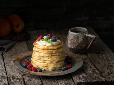 Pancake with vanilla cream, blueberries and raspberries. Dark moody old rustic wooden background.