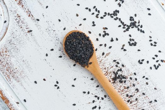 Black Sesame on a wooden spoon. White wooden background. Top view, close up. Copy space.