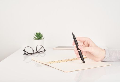 female young hand holding pen and writing on notebook page on white and gray background side view copy space
