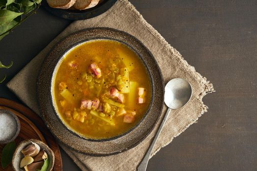 Winter hot soup with chopped green peas, pork, bacon, smoked on a dark brown wooden table. Delicious appetizing fat rich soup, copy space
