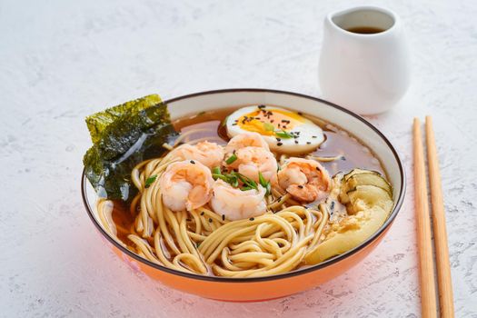 Asian soup with a noodles, ramen with shrimps, miso paste, soy sauce. White stone table, side view