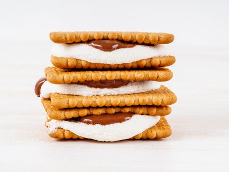 Smores, marshmallow sandwiches - traditional American sweet chocolate cookies on white wooden table, side view.