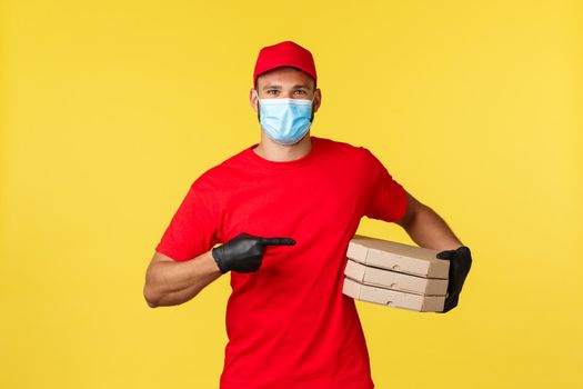 Food delivery, tracking orders, covid-19 and self-quarantine concept. Smiling courier pointing at delicious pizza, bring order to customer home, wear protective gloves and medical mask.