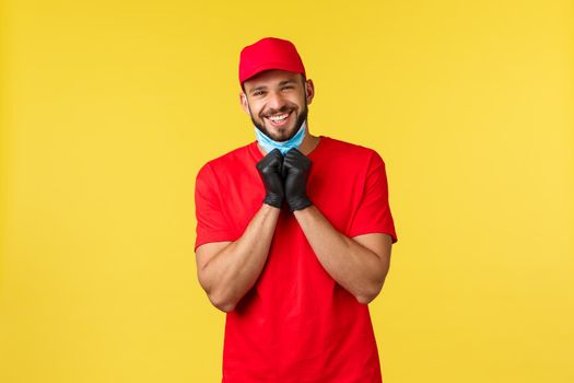 Express delivery during pandemic, covid-19, safe shipping, online shopping concept. Friendly charismatic courier in red uniform, gloves, take-off medical mask to smile sincere, yellow background.